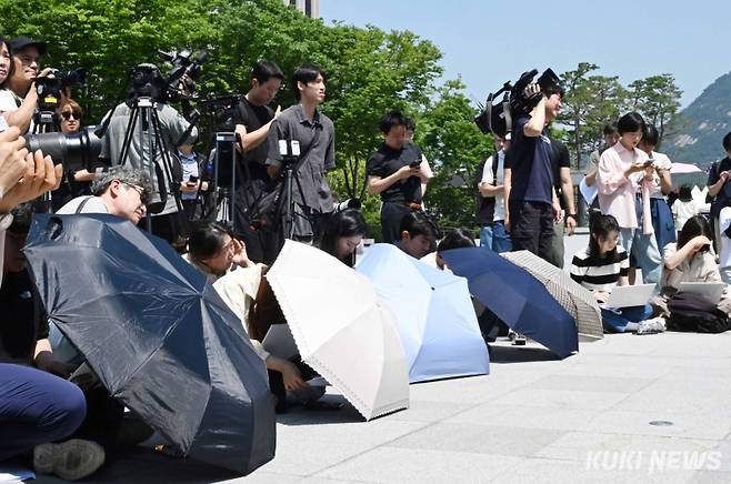 23일 서울의 낮 기온이 32도까지 오르는 등 폭염 속에서 기자들이 바닥에 앉아 양산으로 노트북을 가리고 취재에 열중하고 있다.