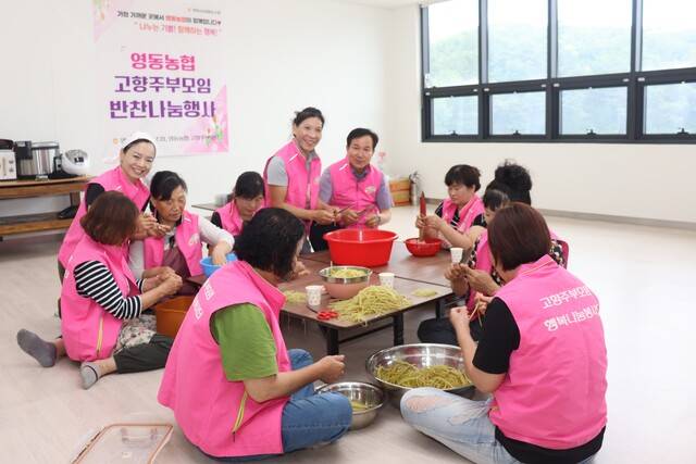 안진우 충북 영동농협 조합장(뒷줄 왼쪽 여섯번째)이 고향주부모임 회원들과 함께 머위대를 다듬으며 지역의 어려운 이웃이게 전달할 반찬을 준비하고 있다.