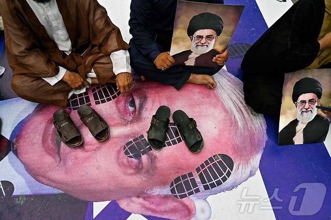 파키스탄의 시아파 무슬림들이 22일(현지시간) 카라치에서 미국과 이스라엘의 이란 공격을 성토하며 이란 최고 지도자 아야톨라 알리 하메네이의 초상화를 들고 있다. 이들은 이스라엘의 베냐민 네타냐후 총리의 사진을 깔고 앉아 있는데 이 사진에는 발자국까이 프린트 되어 있다. 2025.06.22. ⓒ AFP=뉴스1 ⓒ News1 권영미 기자