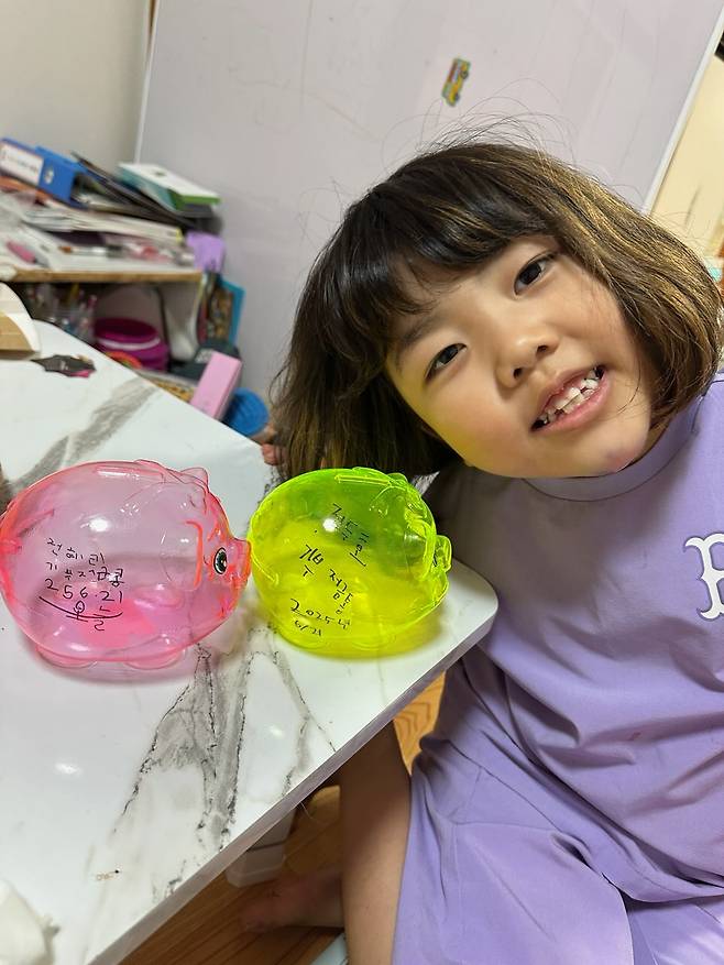 전혜리양이 올해 오빠와 함께 용돈을 모았던 투명한 형광색 돼지 저금통과 함께 웃고 있다. 정혜림씨 제공