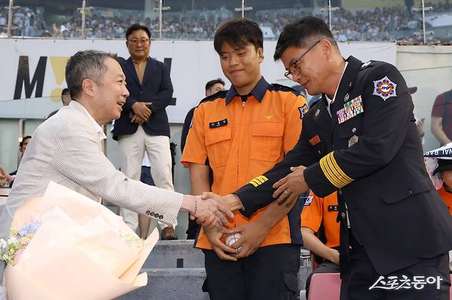 두산 구단주인 박정원 두산그룹 회장(왼쪽)이 24일 잠실구장에서 열린 ‘소방가족 마음돌봄’ 행사에서 시구자 손용원 소방교와 대구지하철 참사 당시 소방 활동에 나선 부친 손진복 소방경에게 꽃다발을 전달하고 있다. 사진제공｜두산 베어스