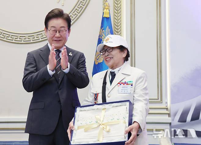 [서울=뉴시스] 최진석 기자 = 이재명 대통령이 27일 청와대 영빈관에서 열린 '호국보훈의 달, 대통령의 초대' 행사에서 특별초청 대상자인 6·25전쟁 참전유공자 이춘자 참전용사에게 광목이불 선물을 전달 후 박수치고 있다. (대통령실통신사진기자단) 2025.06.27. myjs@newsis.com