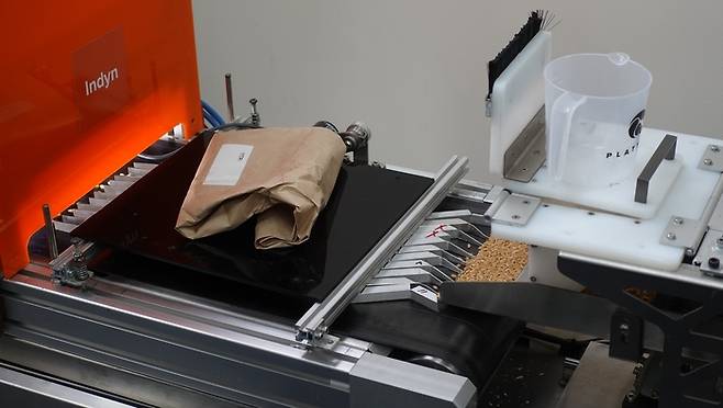 플래티퍼스 비전이 개발한 곡물 품질 검사 장비가 가동되고 있다. 오른쪽으로 투입된 밀알이 컨베이어 벨트를 타고 왼쪽으로 이동해 붉은색 부분 안에 설치된 카메라를 통해 AI로 분석하는 방식이다.