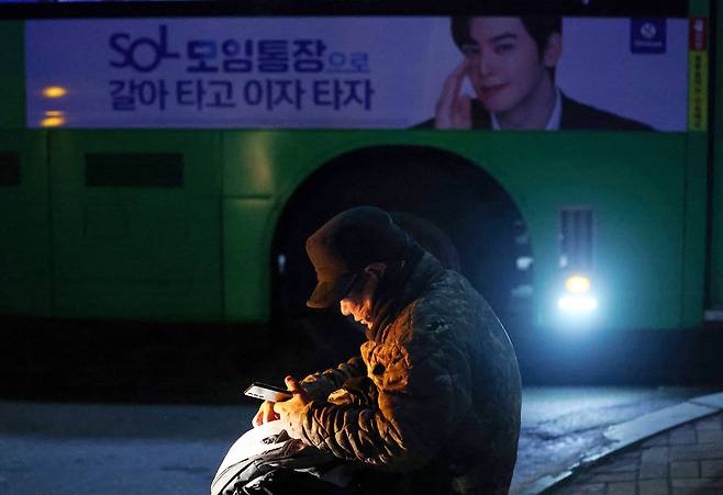 18일 새벽 인력사무소가 밀집한 서울 남구로역 인근에서 일감을 기다리는 일용직 구직자 뒤로 은행 광고가 붙은 버스가 지나고 있다. [연합]