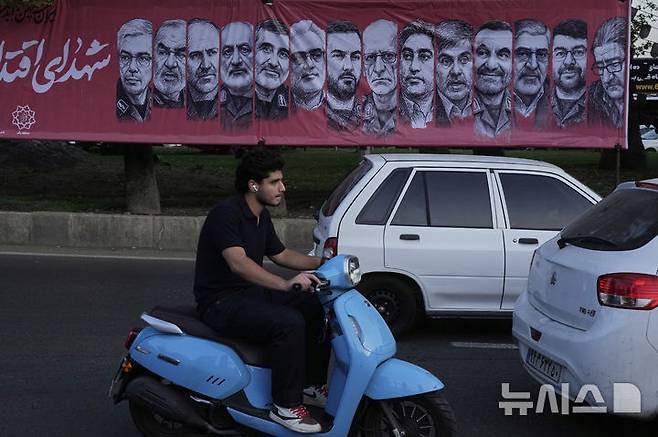 [테헤란=AP/뉴시스] 지난6월 30일 이란 테헤란 북부 타즈리시 광장에서 스쿠터와 차량이 이스라엘의 공습으로 사망한 이란군 지휘관들과 핵 과학자들의 초상이 담긴 현수막 옆을 지나가고 있다. 2025.07.06.