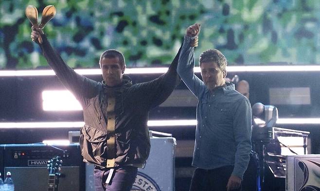 지난 4일(현지시각) 영국 웨일스 카디프 프린시팰리티 스타디움에서 16년 만에 컴백 무대를 펼친 록 밴드 오아시스의 리암 갤러거(왼쪽)가 형 노엘 갤러거의 손을 잡고 번쩍 들어올리고 있다. 카디프/AP 연합뉴스