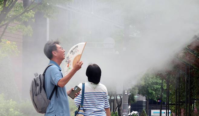 As sweltering weather continues and most parts of Korea remain under heat wave alerts on July 1, a person fans himself in front of a cooling fog system at Seoul Plaza in central Seoul. [YONHAP]