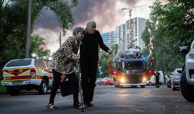 4일(현지시각) 러시아가 우크라이나 키이우에 드론과 미사일 공세를 가하면서, 아파트 뒤로 연기가 피어오르는 가운데 노부부가 길을 건너고 있다. UPI연합뉴스
