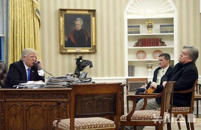 [워싱턴=AP/뉴시스]도널드 트럼프 미 대통령이 1기 시절인 2017년 1월28일(현지시각) 백악관 집무실에서 마이클 플린 국가안보보좌관(가운데)가 스티브 배넌 최고전략고문을 앞에 두고 외국 정상과 통화하는 모습. 트럼프의 최측근이던 두 사람이 제프리 엡스타인 음모론과 관련해 트럼프를 비판하고 있다. 2025.7.15.