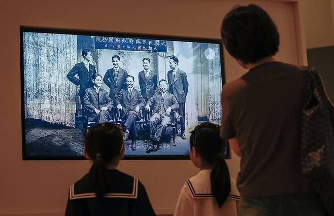 국립중앙박물관과 국사편찬위원회가 특별전 '광복 80주년, 다시 찾은 얼굴들'을 15일 서울 용산구 국립중앙박물관 상설전시관 1층 대한제국실에서 공동 개막한 가운데 전시관 화면에 인공지능(AI) 기술로 구현한 대한민국 임시정부 국무위원들의 미소짓는 영상이 재생되고 있다.