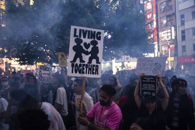 13일 일본 도쿄 신주쿠에서 ‘외국인 규제’를 주장하는 참정당에 반대하는 항의 집회가 열린 가운데 집회에 참가한 외국인이 ‘함께 살자’는 구호가 적힌 피켓을 들고 행진하고 있다./AP 연합뉴스