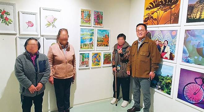 서울시 주최로 지난해 11월 덕수궁 인근 ‘스페이스 소포라’에서 열린 ‘희망의 인문학 수료생 전시회’에서 작품을 출품한 동자동 주민들과 기념사진을 찍는 모습. 서울역쪽방상담소 제공