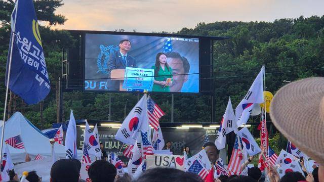 모스 탄(화면 속 남성) 미국 리버티대 교수가 15일 서울대 정문 앞 광장에서 열린 보수단체 트루스포럼 주최 간담회에 참석해 연단에 올라 있다. 국내 지지자들이 태극기와 성조기를 흔들고 있다. 김나연 기자