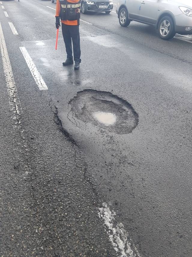 지난 19일 오후 부산 기장군 도로에 깊이 1m의 포트홀이 발생해 소방대원이 차량 통행을 제한하고 있다. 부산소방재난본부 제공