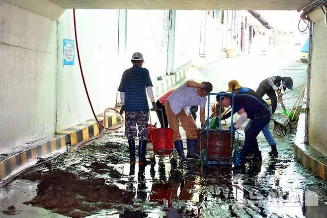 [광주=뉴시스] 이현행 기자 = 양동 공영주차 관리위원회 직원들이 20일 오전 광주 서구 양동전통시장 주차장 입구에서 광주천 범람으로 쌓인 토사물과 수풀을 치우고 있다. 2025.07.20. lhh@newsis.com