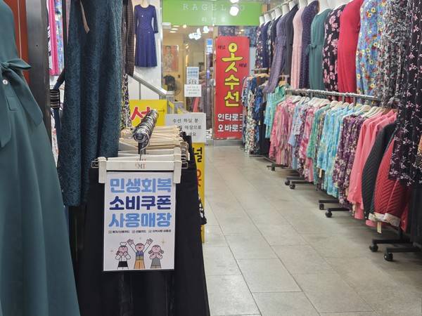 21일 수원 영동시장에서 권점숙씨가 운영하는 옷가게 앞 옷걸이에 '민생회복 소비쿠폰 사용매장' 포스터가 걸려 있다. [사진=김지호 기자]