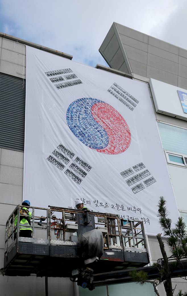 ▲ 제80주년 광복절을 앞두고 22일 오전 수원시 권선구청 외벽에 관계자들이 손도장으로 만든 대형 태극기를 설치하고 있다. /전광현 기자 maggie@incheonilbo.com