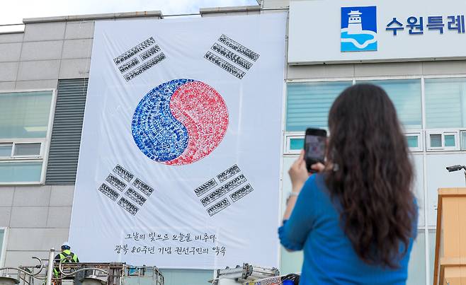 ▲ 제80주년 광복절을 앞두고 22일 오전 수원시 권선구청 외벽에 관계자들이 손도장으로 만든 대형 태극기를 설치하고 있다. /전광현 기자 maggie@incheonilbo.com