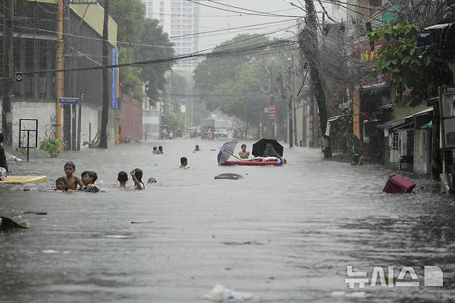 [필리핀=AP/뉴시스] 21일(현지 시간) 필리핀 케손시에서 제6호 태풍 위파 영향으로 몬순 비가 증가한 가운데 주민들이 물에 잠긴 거리를 빠져나가고 있다. 2025.07.22.