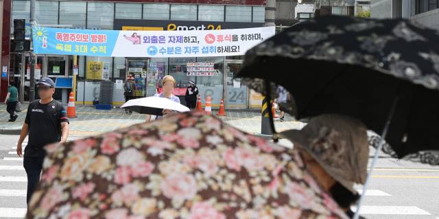 서울 전역에 폭염경보가 발령되는 등 가마솥더위가 이어진 24일 양산을 쓴 시민들이 서울 서대문구 거리에서 폭염시 행동 수칙이 담긴 현수막 앞을 지나고 있다. 금요일인 25일과 토요일인 26일에는 서울의 한낮 최고기온이 각각 37도와 38도까지 오를 것으로 보인다. 오승현 기자