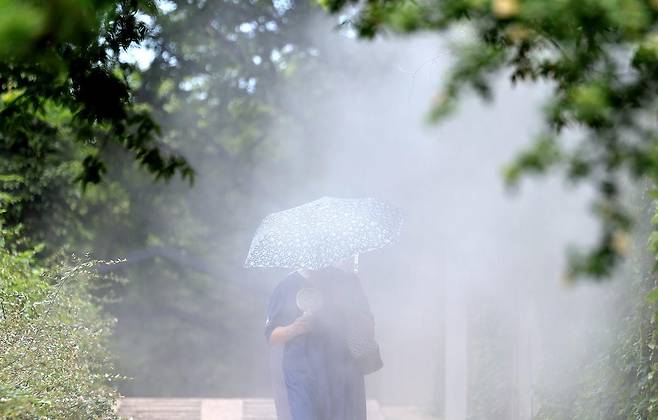 폭염이 연일 계속된 23일 대구 중구 청라언덕에 설치된 쿨링포그 아래로 한 시민이 손 선풍기를 들고 이동하고 있다. 2025.07.23. 뉴시스