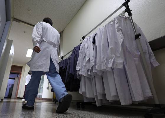 A doctor walks by a hanger with doctors' white gowns at a general hospital in Daegu in March 2024. [YONHAP]