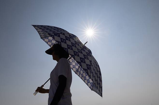 A woman wearing a sun cap and carrying an umbrella walks under the scorching sun near Hanagae Beach in Incheon on July 25, as heat wave warnings are in effect across most of the country. [CHOI GI-UNG]