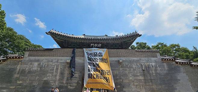경복궁 영추문에 내걸린 전장연 대형 현수막 (서울=연합뉴스) 경복궁 영추문에 장애인 권리 보장을 요구하는 대형 현수막을 내건 전국장애인차별철폐연대(전장연) 활동가들이 경찰에 현행범 체포됐다.
    25일 경찰과 전장연에 따르면 전장연 활동가 3명은 이날 낮 12시 20분께 서울 종로구 경복궁 영추문 위로 올라가 '권리 중심 중증장애인 맞춤형 공공일자리 확대하라'는 구호가 적힌 대형 현수막을 내걸었다. 현수막은 현재 모두 철거된 상태다.  2025.7.25  [전국장애인차별철폐연대(전장연) 제공. 재판매 및 DB 금지] photo@yna.co.kr