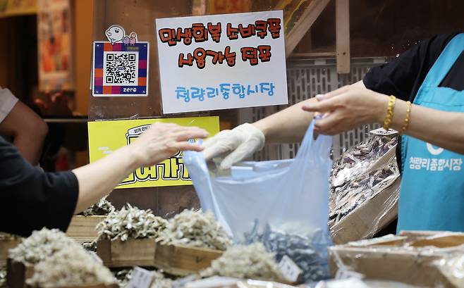 A customer shops at Cheongyangni Traditional Market in Dongdaemun District, eastern Seoul, on July 25, as a sign indicates the store accepts government-issued consumption vouchers. [NEWS1]