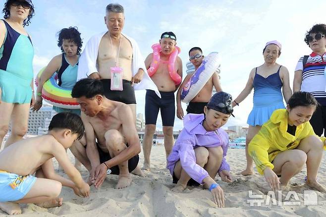 [원산=AP/뉴시스] 북한의 올해 상반기(1~6월) 비치파라솔 등 리조트 관련 용품 수입이 급증한 것으로 조사됐다. 갈마반도 갈마 해안관광지구가 완공된 영향으로 보인다. 사진은 지난 2일 북한 강원도 원산의 원산-갈마 해안관광지구에서 어린이들이 모래사장에 '우리 조국'이라고 쓰는 모습을 어른들이 지켜보고 있는 모습. 2025.07.29.