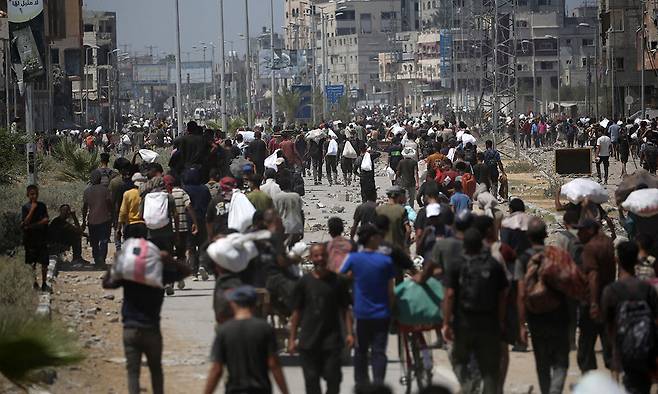 27일(현지시간) 가자지구 중부 넷자림 통로 인근에 위치한 미국 주도의 가자인도주의재단(GHF) 배급소에서 식량 등 구호품을 지급받은 팔레스타인인들이 짐을 짊어지고 누세이라트 난민 캠프로 복귀하고 있다. 가자지구=AFP연합뉴스