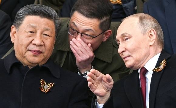 2025년 5월 9일(현지시간) 러시아 모스크바 붉은광장에서 열린 전승절 80주년 열병식을 참관하는 시진핑(왼쪽) 중국 국가주석이 블라디미르 푸틴(오른쪽) 러시아 대통령과 통역을 사이에 두고 대화를 나누는 모습.  UPI 연합뉴스