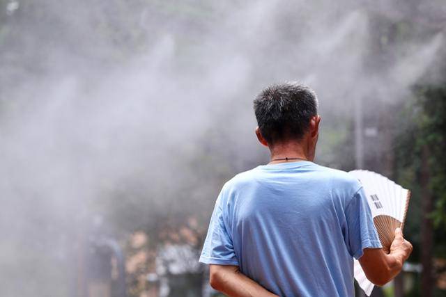 서울 한낮 기온이 34도까지 치솟으며 무더운 날씨를 보인 24일 서울역 쪽방촌 인근 한 공원에서 주민이 쿨링포그를 맞으며 부채질을 하고 있다. 연합뉴스