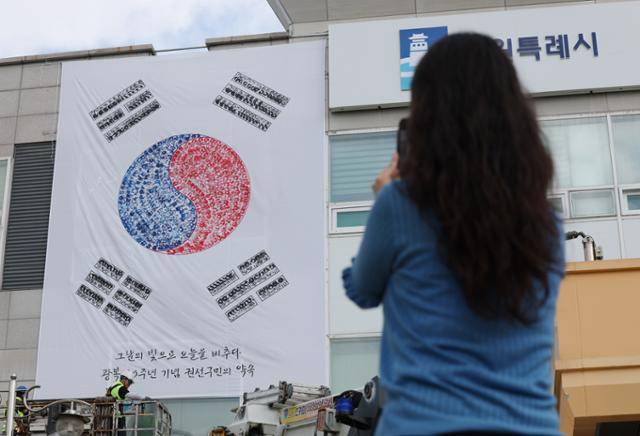 한 여성이 지난달 22일 경기 수원시 권선구청 외벽에 설치된 태극기 사진을 찍고 있다. 뉴스1