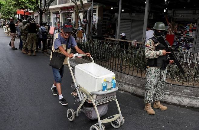 치안이 불안하기로 알려진 에콰도르 수도 키토에서 한 시민이 무장한 군 장병 옆을 지나가고 있다. [AFP]