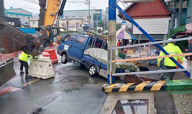 부산 사상구 감전동 새벽시장 앞 도로에 발생한 싱크홀에 빠진 1t 트럭을 굴착기를 이용해 구조하고 있다. 부산소방재난본부&nbsp;제공