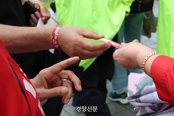 전당대회장 외부에서 한 당원이 무작위로 희망자에게 입장 띠지를 나눠주고 있다. 한수빈 기자