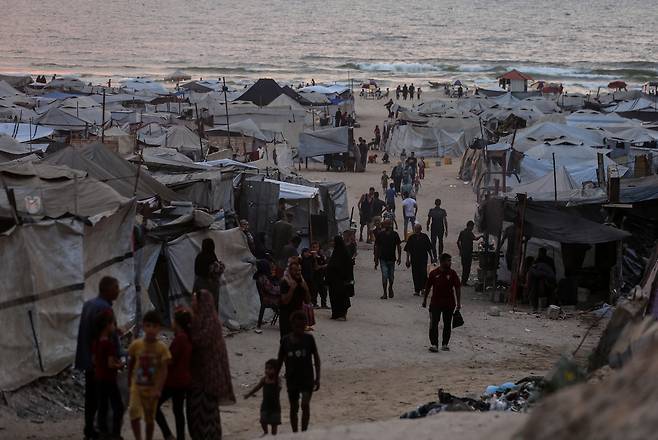 12일(현지시간) 가자시티의 한 해변가에서 팔레스타인 피란민을 위한 천막 옆을 사람들이 지나가고 있다. 신화연합뉴스