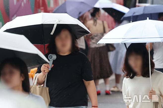 [서울=뉴시스] 권창회 기자 = 수도권을 비롯한 중부지역에 호우가 예보된 6일 서울 종로구 광화문광장에서 시민들이 우산과 선풍기를 들고 이동하고 있다. 2025.08.06. kch0523@newsis.com