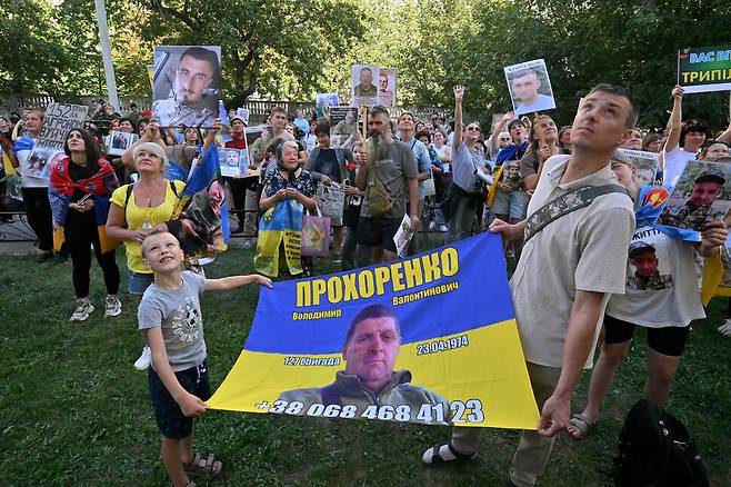 14일(현지시각) 체르니히우 지역에서 전쟁 포로(POW) 교환으로 석방된 이들이 있는 건물을 향해 우크라이나 시민들이 실종되거나 체포된 친척과 친구의 초상화를 들고 있다. 체르니히우/AFP 연합뉴스