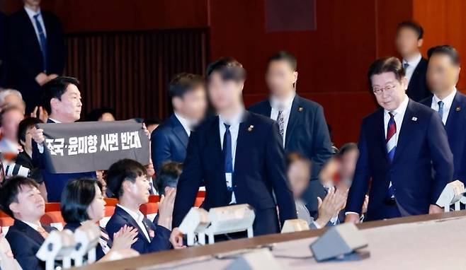 15일, 안철수 국민의힘 의원(왼쪽)이 광복절 경축식장에서 ‘조국·윤미향 사면 반대’ 펼침막을 들고 기립 시위하고 있다. 바로 앞을 이재명 대통령(오른쪽)이 경호 인력과 함께 지나가고 있다. (안 의원 페이스북 캡처)