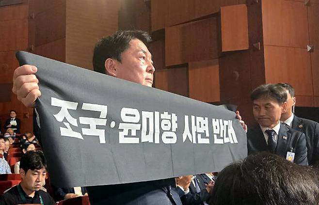[서울=뉴시스] 조성봉 기자= 안철수 국민의힘 당대표 후보가 15일 오전 서울 종로구 세종문화회관에서 열린 제80주년 광복절 경축식에서 경축사 중인 이재명 대통령을 향해 ‘조국, 윤미향 사면 반대’ 플래카드를 들어보이며 항의하고 있다. 안철수 캠프 제공