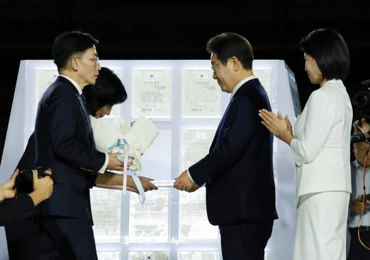 이재명 대통령과 김혜경 여사가 지난 15일 서울 세종대로 광화문광장에서 열린 제21대 대통령 국민임명식 '광복 80년, 국민주권으로 미래를 세우다' 행사에서 국민대표인 이국종 국군대전병원장과 이연수 NC AI 대표로부터 '빛의 임명장'과 꽃다발을 받고 있다. 연합뉴스