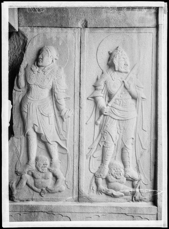 석굴암 석실 내 벽면에 새겨진 사천왕상 중 다문천왕(多聞天王)과 지국천왕(持國天王)의 부조다. 두 천왕은 무장을 갖춘 위엄 있는 모습으로 조각되어 있으며, 발 아래에는 악귀를 짓밟고 있는 형상이 표현되어 있다. 이는 불법(佛法)을 수호하고 사악한 기운을 물리치는 호법신의 위용을 나타내며, 석굴암 공간 전체가 신성한 불국토임을 상징하는 중요한 시각 요소다. 조각의 세밀함과 균형 잡힌 구도는 통일신라 불교 조각의 정수라 할 수 있다. /중앙박물관e뮤지엄, 건판13036