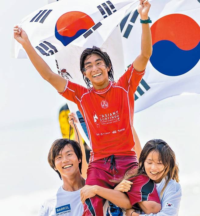 카노아 희재가 지난 11일 아시아 서핑 챔피언십 2관왕에 오른 뒤 태극기를 흔들며 환호하고 있다. 대표팀 동료 목하진(왼쪽)과 김비주(오른쪽)가 팔로 가마를 태워주며 함께 기뻐하고 있다./양양군