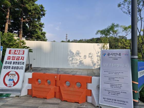 지난달 25일 오후 서울 예장공원에 설치된 높다란 공사 가림막 앞에 남산 곤돌라 설치공사를 알리는 입간판이 놓여 있다. ‘빠른 시일 내에 공사를 마무리하겠습니다’라고 쓰여 있으나 1년째 공사가 중단된 상태다. 백일현 기자