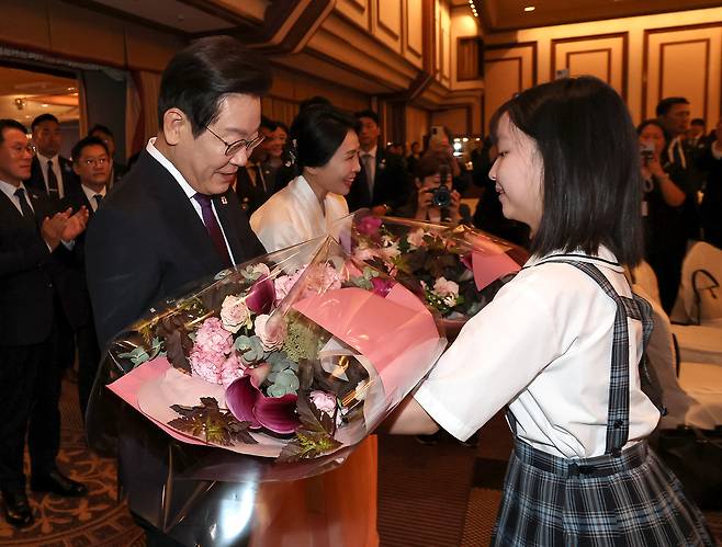 President Lee Jae Myung, left, and first lady Kim Hea Kyung receive flowers from children during a luncheon meeting with the Korean community in Japan at a hotel in Tokyo on Aug. 23. [JOINT PRESS CORPS]