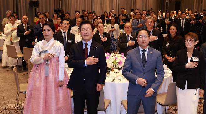 이재명 대통령 부부, 재미동포 만찬 간담회 참석 - 이재명 대통령과 김혜경 여사가 24일(현지시간) 미국 워싱턴DC의 한 호텔에서 열린 동포 만찬 간담회에서 국기에 경례하고 있다. 이 대통령 오른쪽은 앤디 김 미국 상원의원.  워싱턴DC 연합뉴스