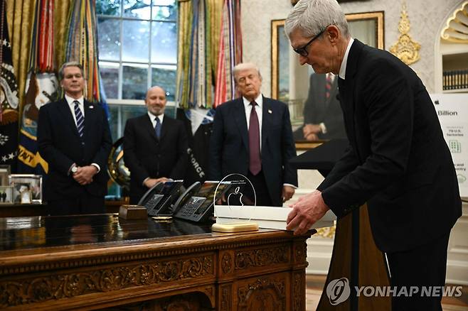 팀 쿡 애플 최고경영자(CEO)가 지난 6일(현지시간) 백악관에서 애플 로고와 자신의 서명이 담긴 '미국산' 유리 기념패를 순금 받침대에 올려 도널드 트럼프 미국 대통령에게 선물하고 있다. 쿡 CEO는 이날 첨단소재·유리 제조업체인 코닝 등을 포함해 미국 내 생산시설에 1천억 달러(약 140조원)를 투자하겠다고 발표했다. [AFP=연합뉴스 자료사진]