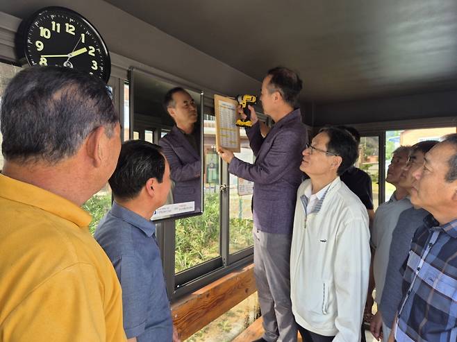 문경시 동로면 두클럽 회원들이 버스 승강장에 버스 시간표, 시계, 거울을 설치하는 모습. /문경시 제공